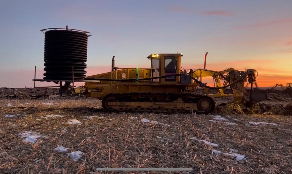 Yellow BRON tiling plow laying drainage tile in an Iowa farm field at sunset Yellow BRON tiling plow laying drainage tile in an Iowa farm field at sunset